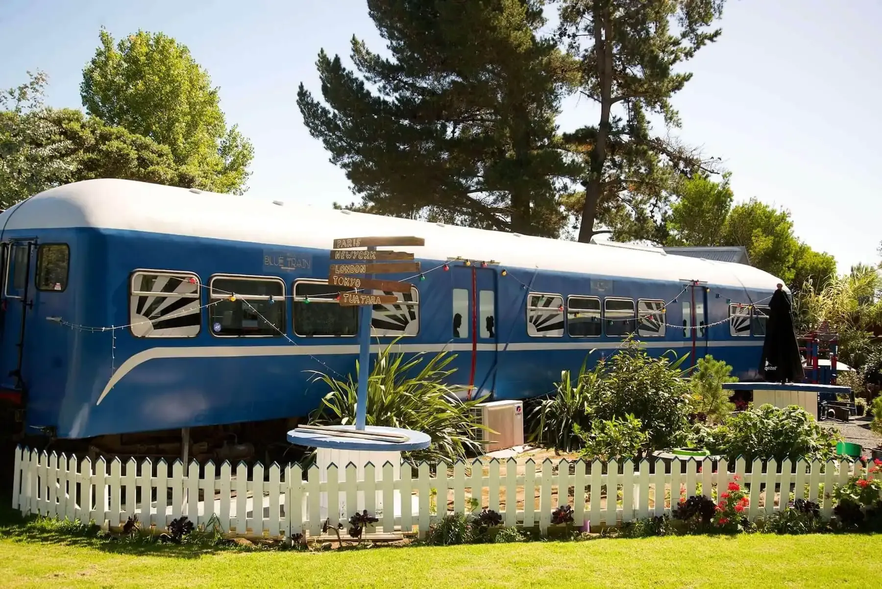 The Blue Train carriage behind a white picket fence and garden in sunshine
