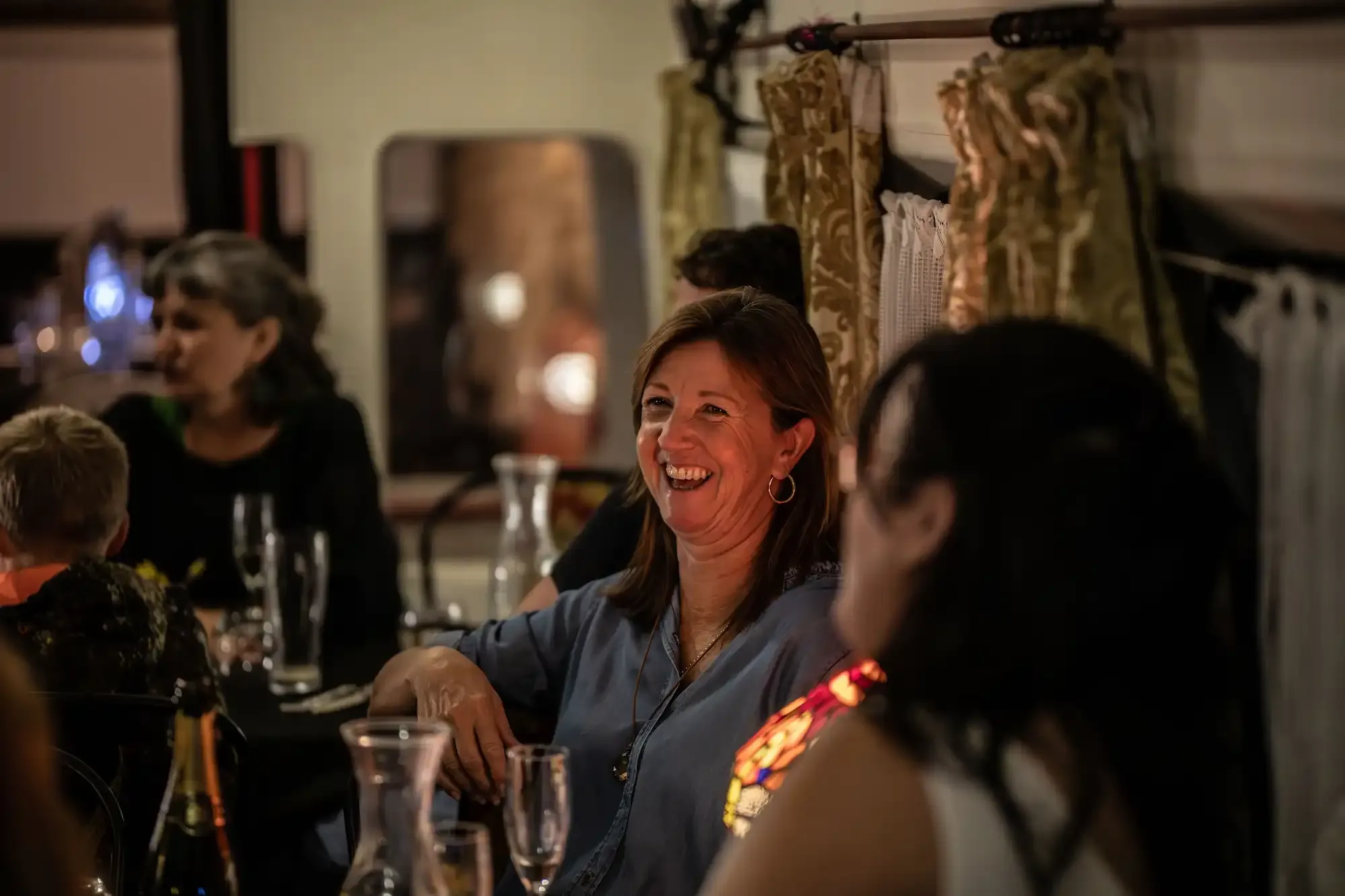 Guests laughing over dinner in the lamplit Blue Train during the Tūī Tour dinner experience on the Kāpiti Coast