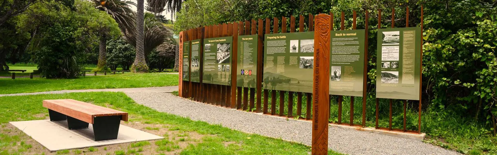 Heritage interpretation panels beside a gravel path and bench in a park